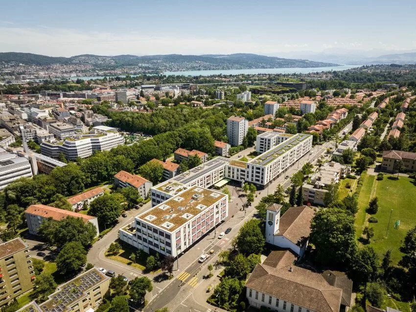 Luftaufnahme der Mehrfamilienhäuser der FGZ-Siedlung Quartierzentrum Friesenberg, dahinter ersichtlich der Zürichsee