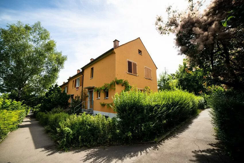 Orangene Reihen-Einfamilienhäuser aus der FGZ-Siedlung Staffelhof (Etappe 4), eingefasst von einer grünen Hecke