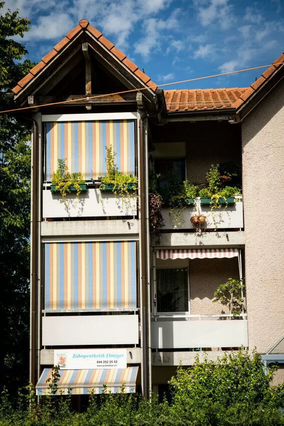 Teilaufnahme von 2 Stöcken eines Mehrfamilienhauses der Siedlung Schweighofstrasse Mitte (Etappe 7), sichbar sind zwei Balkone mit bunten Rolläden