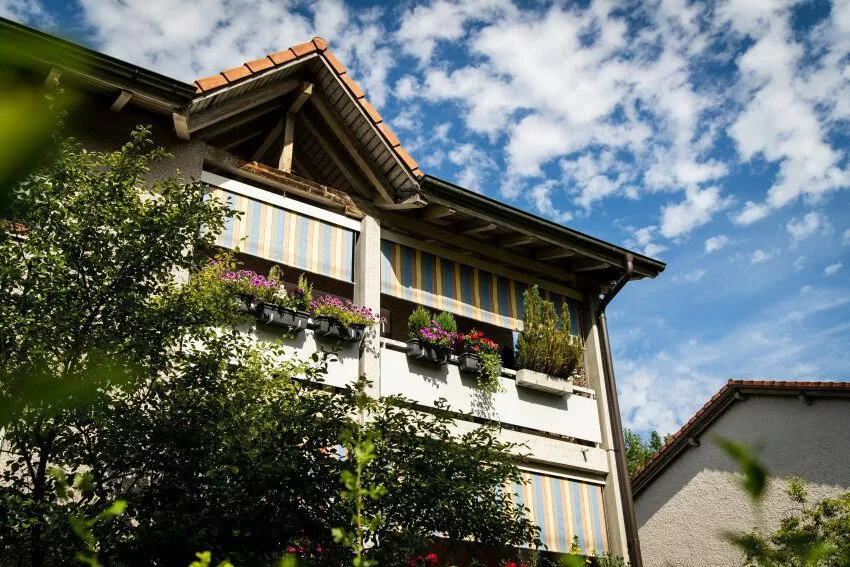 Teilaufnahme vom obersten Stock eines Mehrfamilienhauses der Siedlung Schweighofstrasse Mitte (Etappe 7), sichtbar ist der Balkon mit Rolladen und Himmel hinter dem Haus
